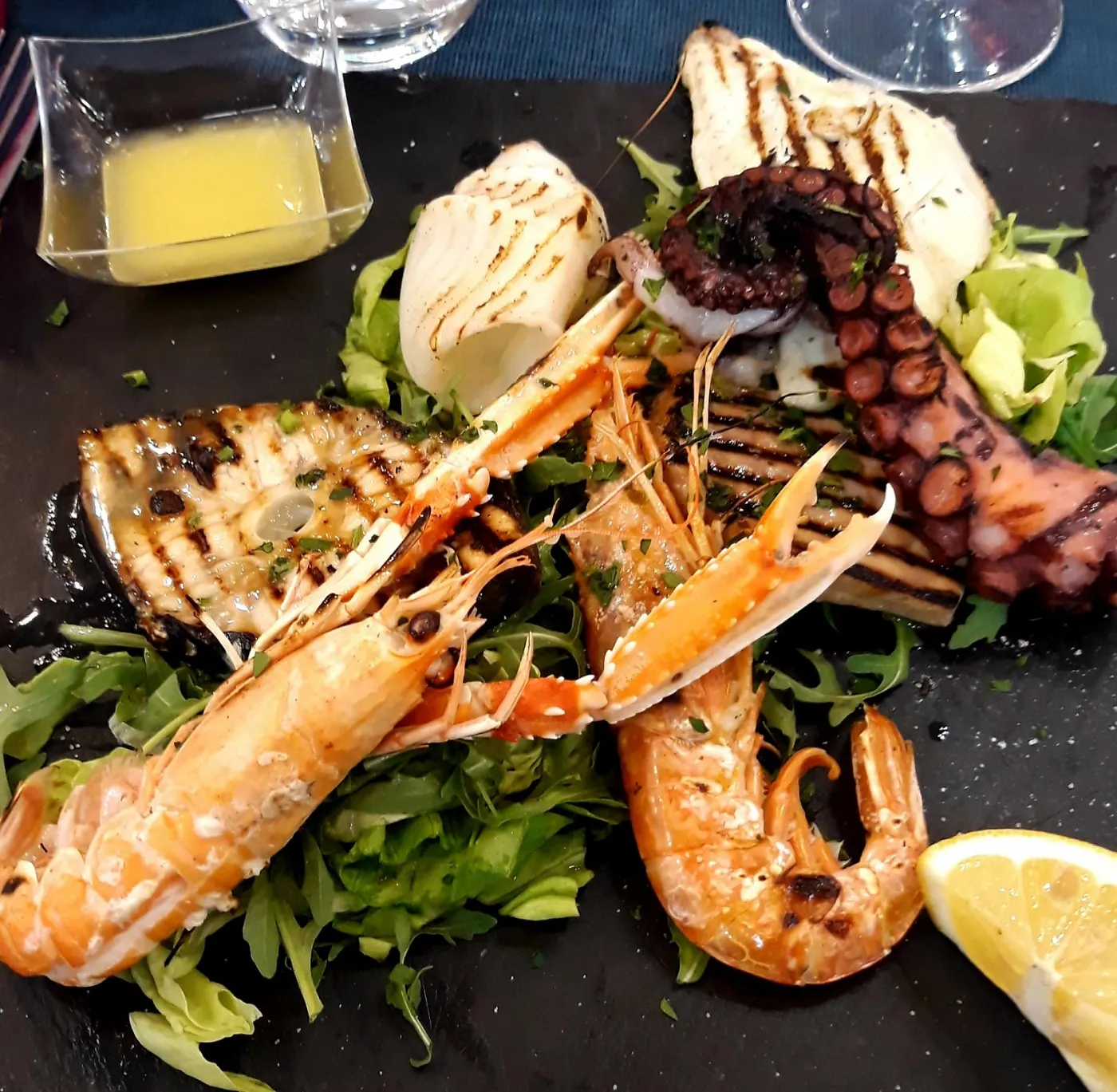 Grigliata mista di pesce servita su ardesia: gamberi, scampi, polpo, calamari e pesce