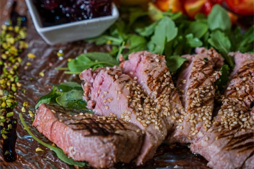 Tagliata al sesamo su letto di rucola, pomodorini e salsa ai frutti di bosco